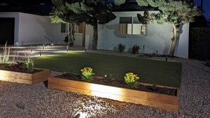 Ein modernes Haus mit einem gut beleuchteten Garten, einer gepflasterten Auffahrt und einer weißen Fassade.