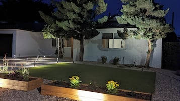 Une maison moderne dotée d’un jardin bien éclairé, d’une allée pavée et d’une façade blanche.