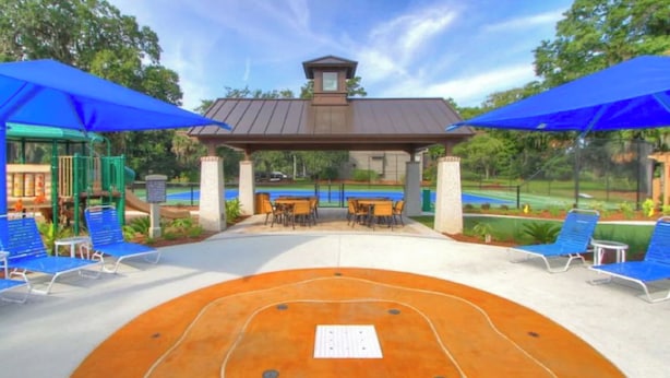 Un área de estar al aire libre con sombrillas azules, una pérgola y una piscina al fondo.