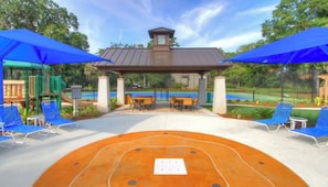 An outdoor seating area with blue umbrellas, a pergola, and a pool in the background. - Spinnaker at Shipyard, 2-bedroom, 2.5 bath townhome (Hilton Head Island)