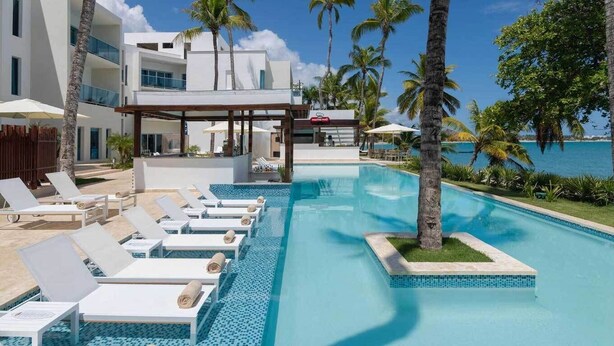 Un área de piscina con sillones de descanso, un espacio cubierto para sentarse y vista al océano.