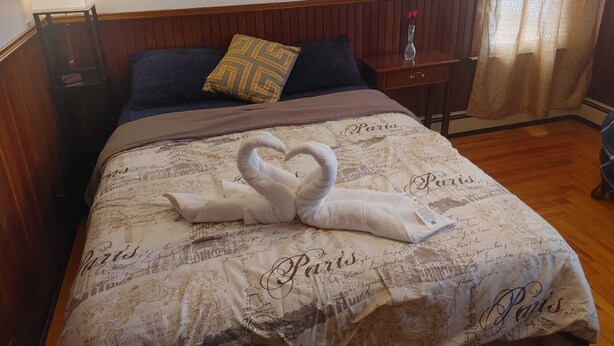 Hotelkamer met bed, nachtkastje, lamp, houten hoofdeinde, raam met gordijnen en decoratief kussen.