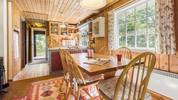 Interior acogedor de una cabaña de madera con comedor, cocina y ventanas amplias.