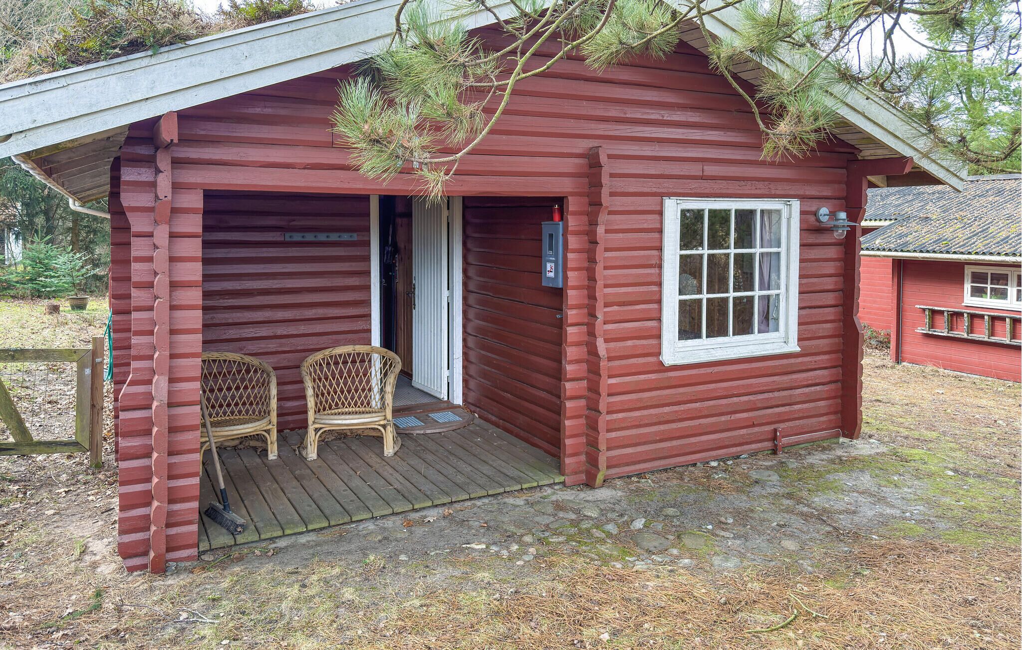A small wooden cabin with a porch, two wicker chairs, and a window.
