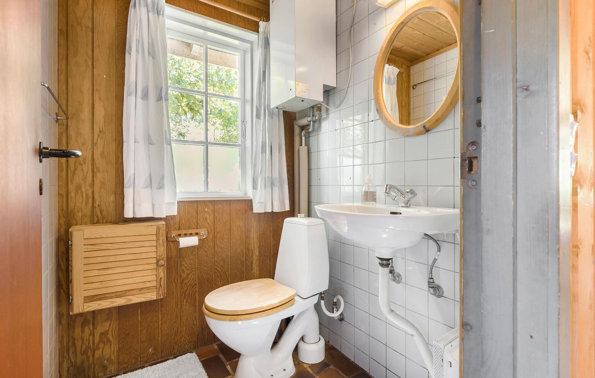 Une salle de bain avec un meuble-lavabo en bois, des toilettes, un lavabo et une fenêtre avec des rideaux.
