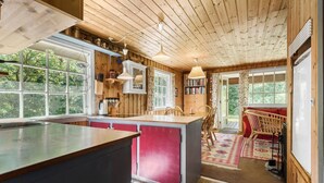Interior de una cabaña de madera con cocina, comedor y vistas al exterior.