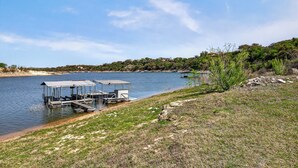 Um píer à beira do lago com área de estar coberta, cercado por margens gramadas e árvores.