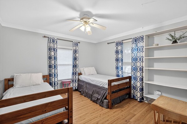 A bedroom with two wooden beds, a ceiling fan, a small table, and a bookshelf.