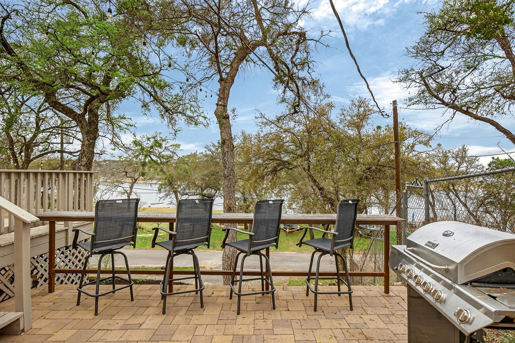 An outdoor patio with three chairs, a grill, and a view of trees and a body of water.