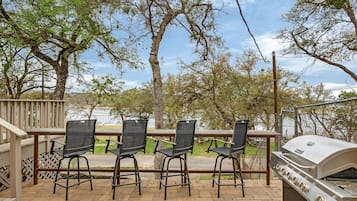 An outdoor patio with three chairs, a grill, and a view of trees and a body of water.