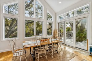 Un coin repas avec une table et des chaises en bois, de grandes fenêtres et une vue sur les arbres.