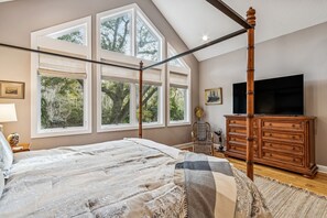 Une chambre à coucher avec un lit à baldaquin, de grandes fenêtres, une télévision et une commode en bois.