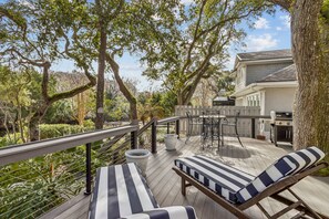 Une terrasse avec des chaises longues, un barbecue et une vue sur la maison.