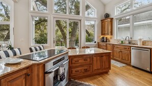 A kitchen with large windows, wooden cabinets, a stainless steel dishwasher, and a granite countertop. - Natures Canopy - Hosted by Moore AI Rentals (Fernandina Beach)