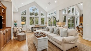 A spacious living room with a large sofa, a dining table, and a kitchen area. - Natures Canopy - Hosted by Moore AI Rentals (Fernandina Beach)