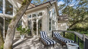 A deck with two lounge chairs, a potted plant, and a house with large windows. - Natures Canopy - Hosted by Moore AI Rentals (Fernandina Beach)