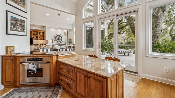 A spacious kitchen with a large island, wooden cabinetry, and a view of the outdoors through large windows. - Natures Canopy - Hosted by Moore AI Rentals (Fernandina Beach)