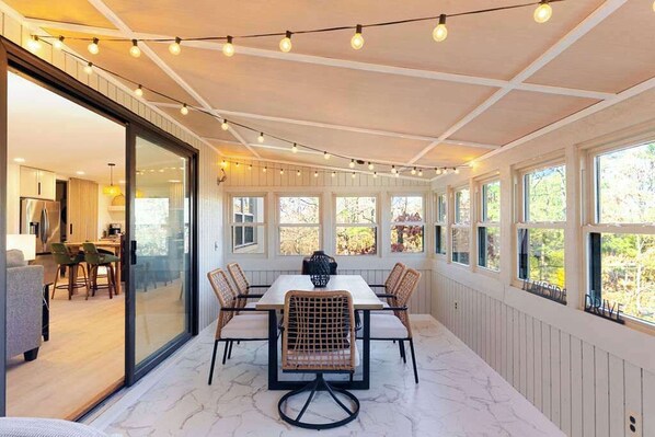 A dining area with a table and chairs, large windows, and string lights.