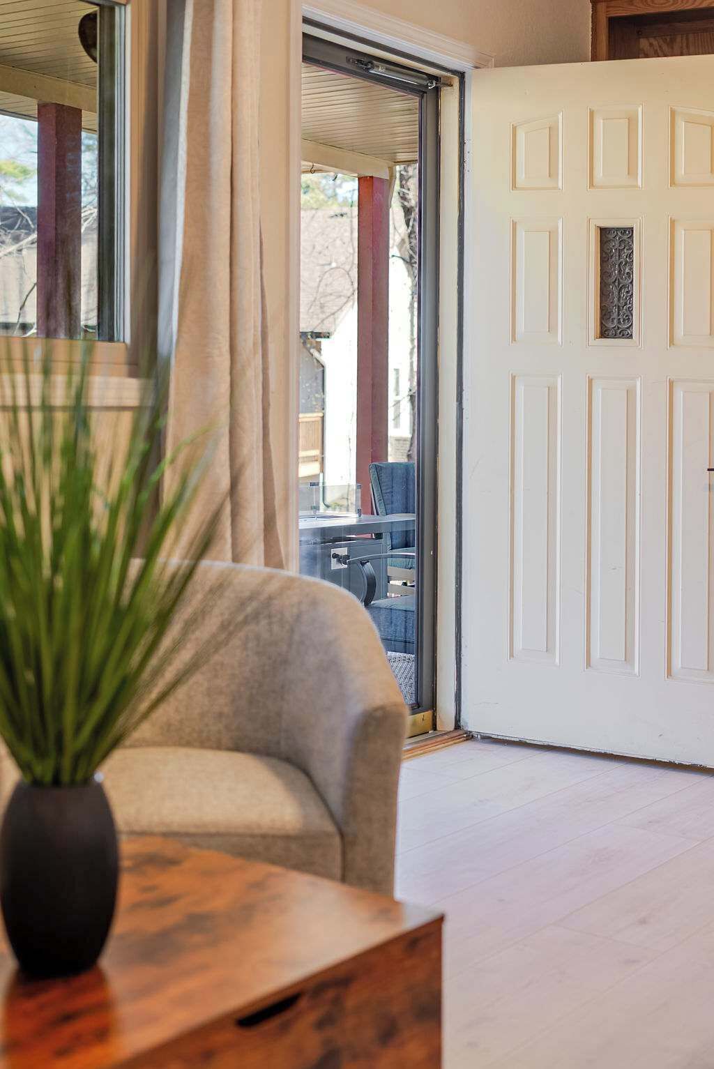 A room with a sliding glass door, a sofa, a small table with a plant, and a view of the outside.