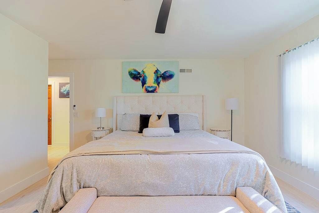 Un dormitorio con cama, un cuadro en la pared y una ventana con cortinas.