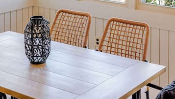 A dining area with a wooden table, wicker chairs, a black vase, and multiple windows with natural light.