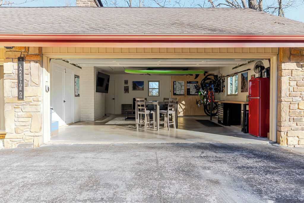 A garage with a concrete floor, a dining table with chairs, a red refrigerator, and a bicycle rack.