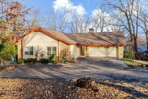 A single-story house with a garage, surrounded by trees and a gravel driveway.