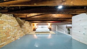 Una camera da letto con un letto, travi in legno, parete in mattoni e una porta bianca.