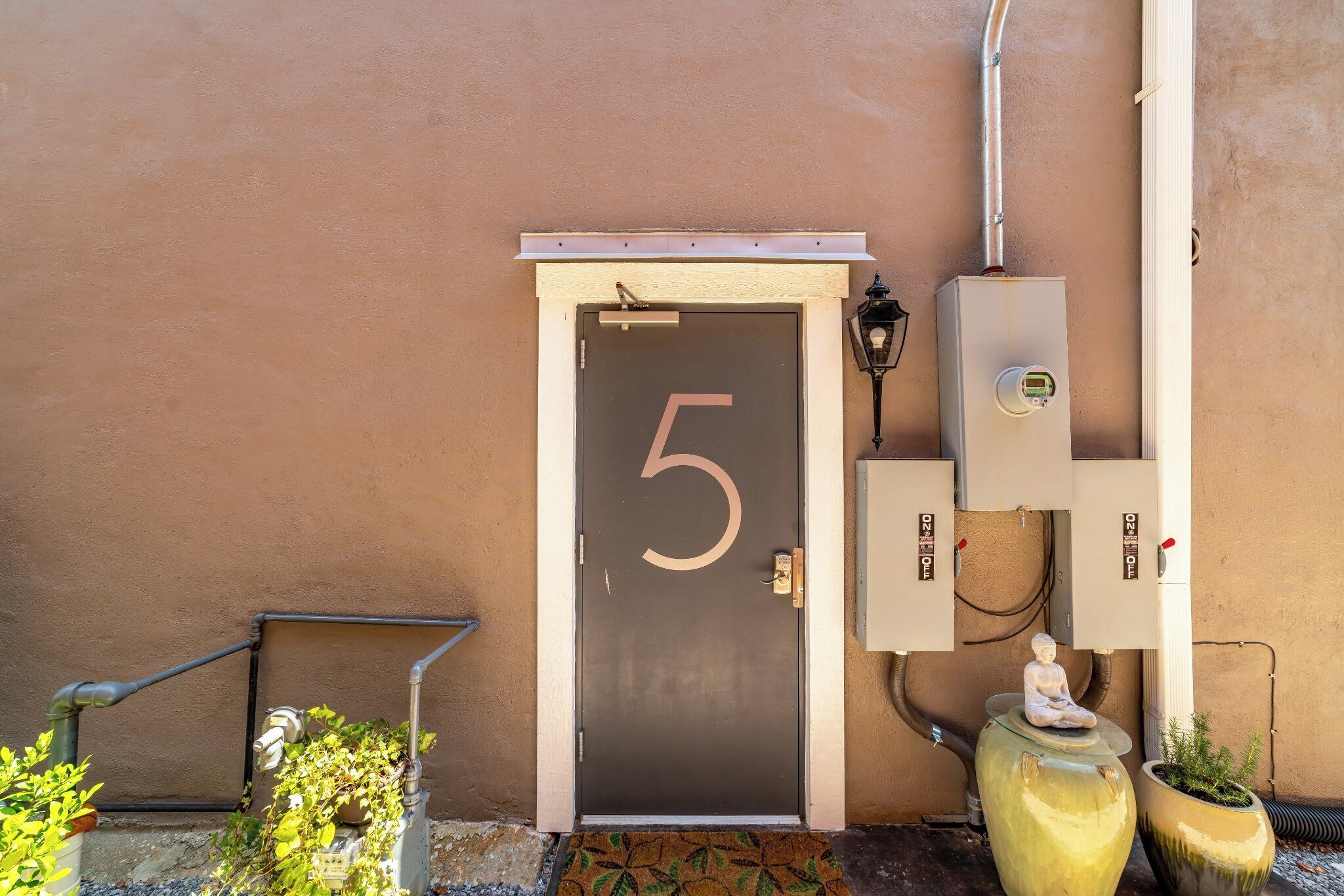 A door with the number 5, outdoor electrical boxes, and a statue on the wall.