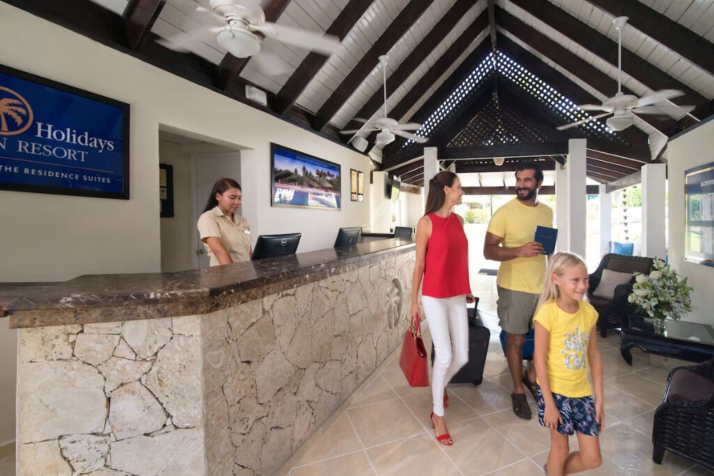 Una zona de recepción con mostrador de piedra, ventilador de techo y cartel que dice 'Holidays Resort'.