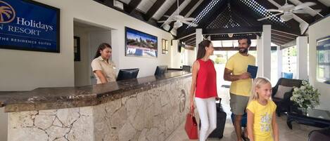 Una zona de recepción con mostrador de piedra, ventilador de techo y cartel que dice 'Holidays Resort'.