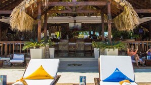 A covered outdoor seating area with lounge chairs, a bar, and potted plants.