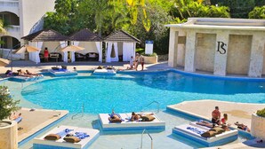 A pool area with lounge chairs, a small pool, and a building with columns.