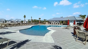 Ein Swimmingpool mit Liegestühlen und Sonnenschirmen, umgeben von einem Zaun und Palmen.