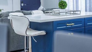 A modern kitchen with a bar area, a flat-screen TV, a dark blue door, and a 'Welcome' sign.