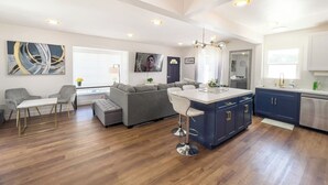 A modern kitchen with a bar area, a dining table, and a sofa in a bright living room.