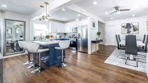 A modern kitchen with a central island, bar stools, and a dining area with a table and chairs.