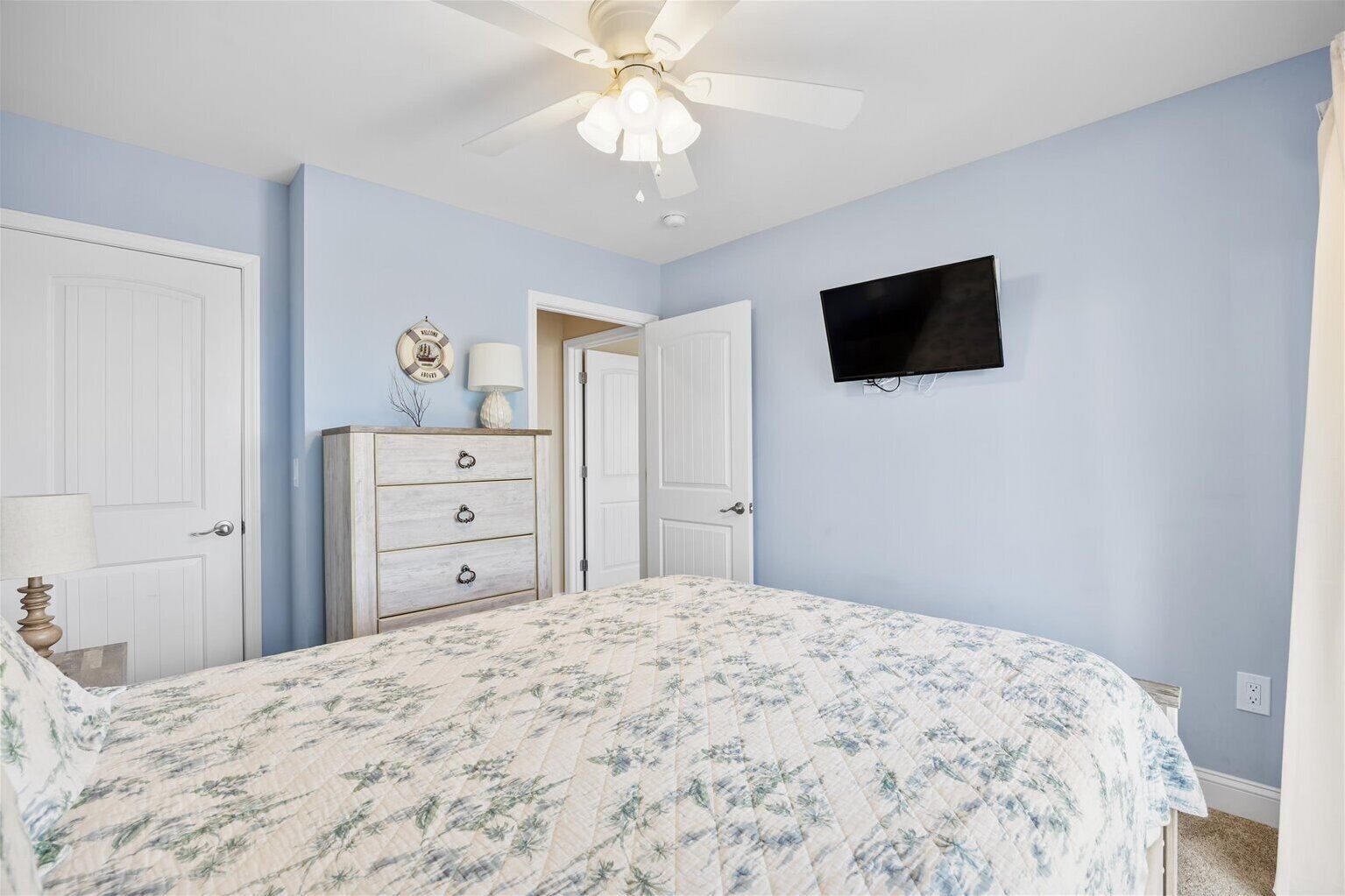 A bedroom with a bed, a dresser, a ceiling fan, a TV, and a door.