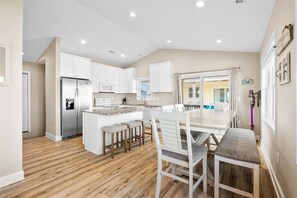 A modern kitchen with white cabinets, a central island, and a dining area with a table and chairs. - Private POOL + Stunning Ocean Views in Heart of Surf City! (Surf City)