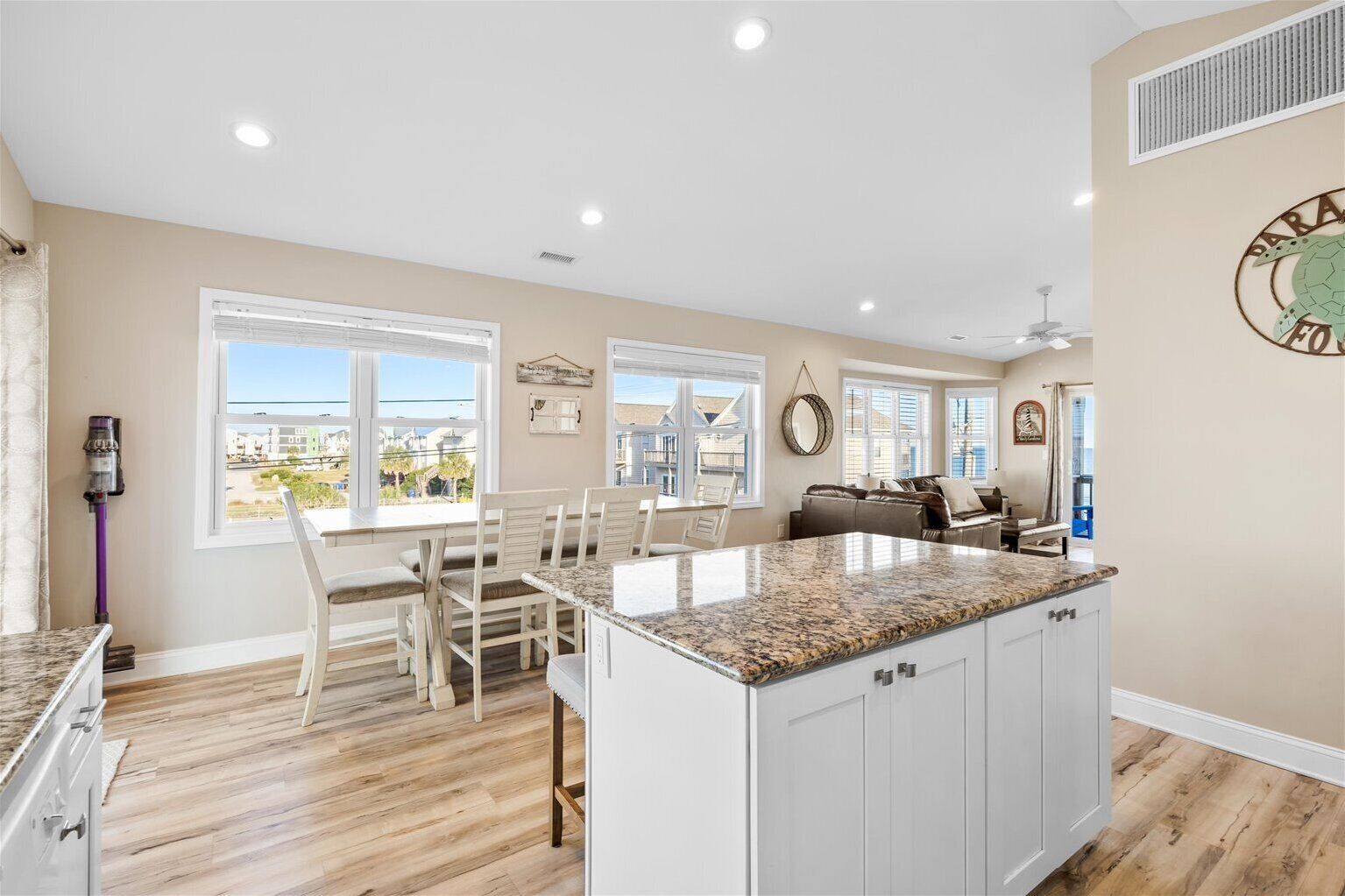 A kitchen with a granite countertop, white cabinetry, and a dining area with a table and chairs.
