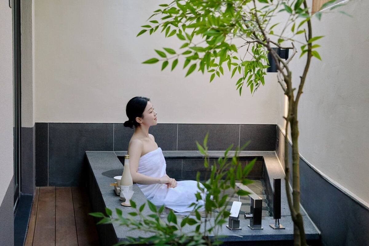 A person in a towel sitting on a bench in a spa-like setting with a small table and a bottle.