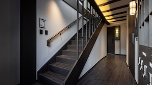 Eine moderne Treppe mit Holzgeländer und dunklen Holzwangen, die zu einem Raum mit Tür und Wandleuchte führt.
