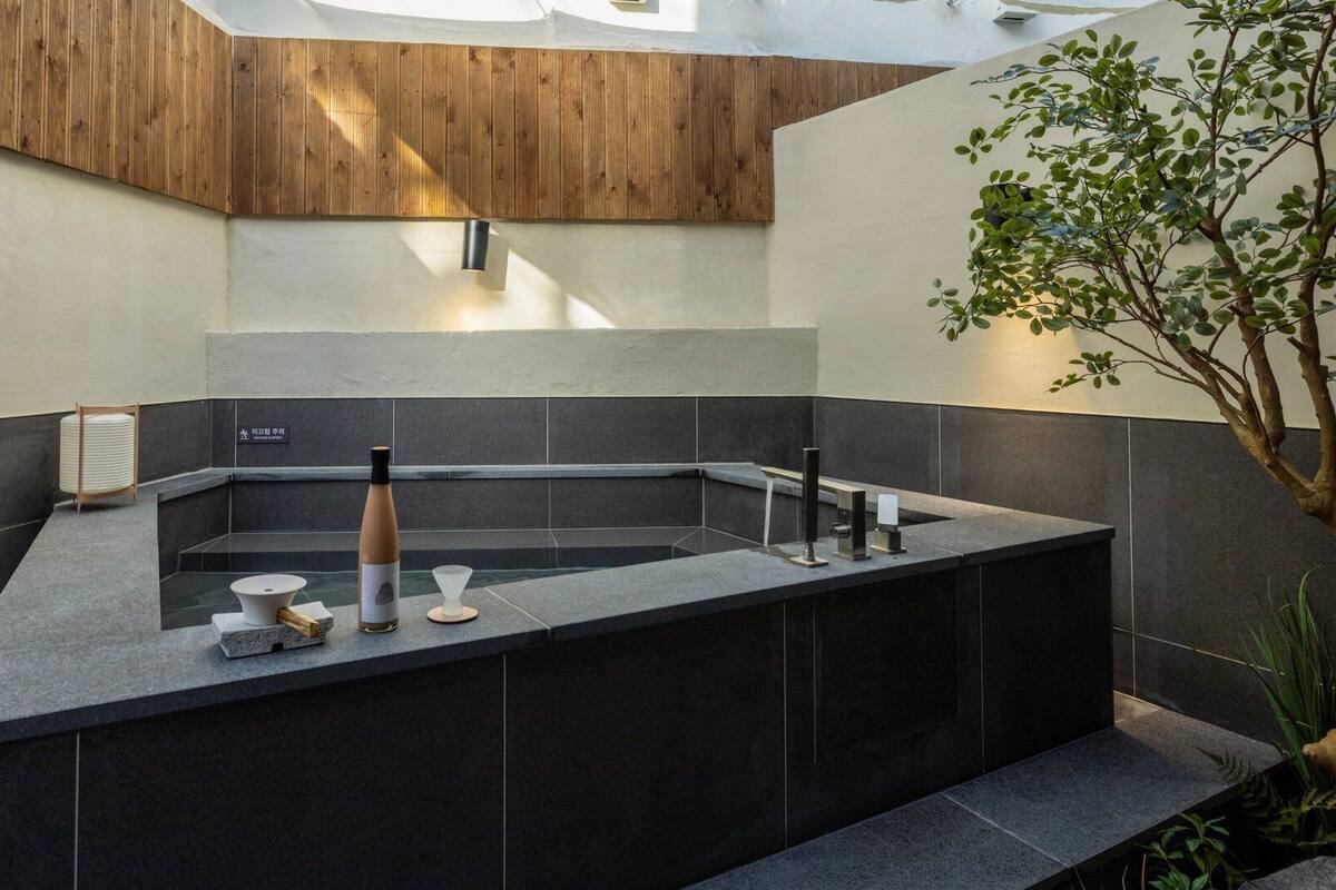 A modern bathroom with a freestanding bathtub, a wooden panel wall, and a small plant.