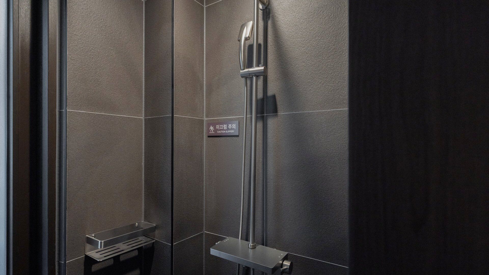 Un baño moderno con ducha, un cartel de precaución para zapatillas y un lavamanos pequeño.