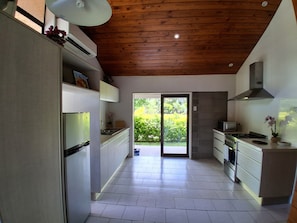 A modern kitchen with wooden ceiling beams, a large sliding glass door leading to a garden, and a built-in stove.