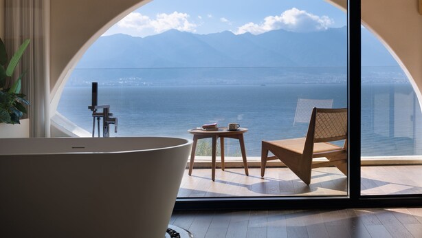 Une pièce dotée d’une grande fenêtre en arc de cercle, d’une baignoire, d’une chaise et d’une petite table.