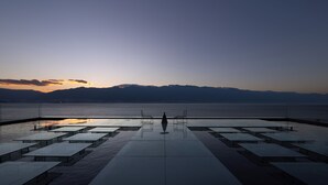 Une terrasse avec des tables et des chaises, offrant une vue sur une étendue d’eau et sur des montagnes lointaines.
