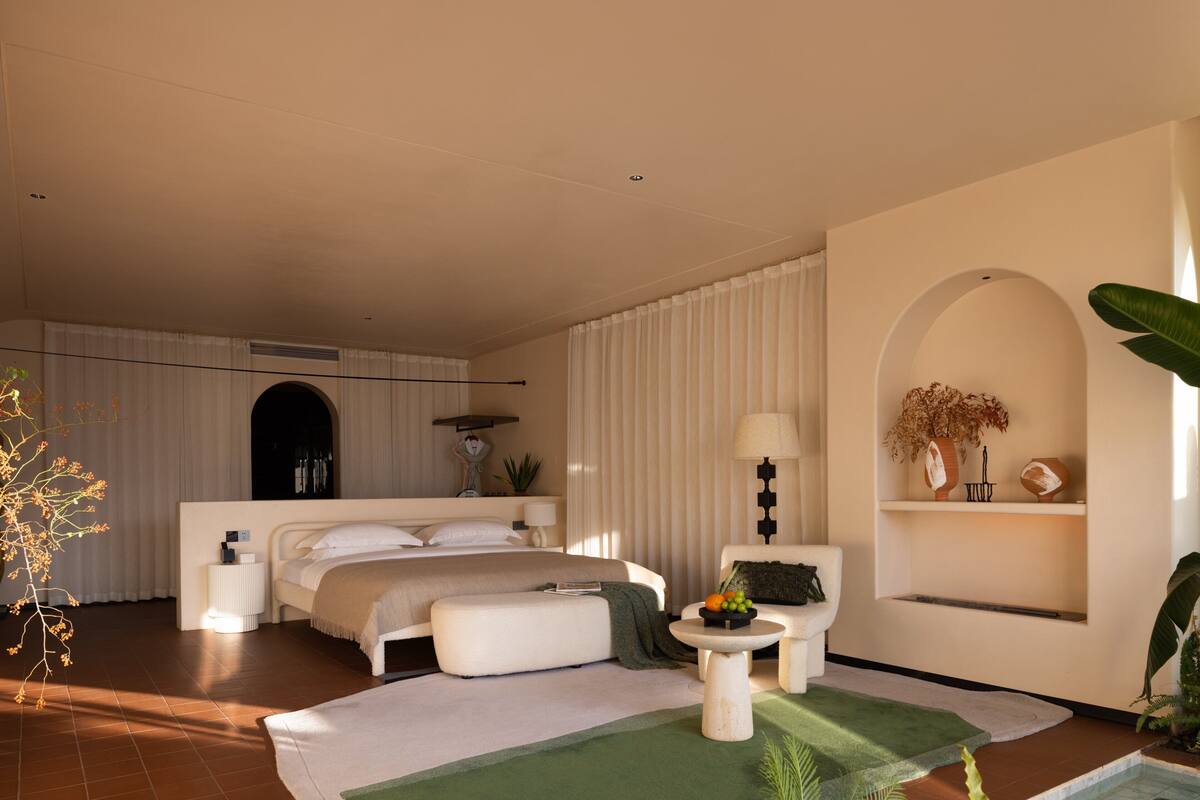 A modern bedroom with a large bed, bedside tables, a small seating area, and a decorative plant.