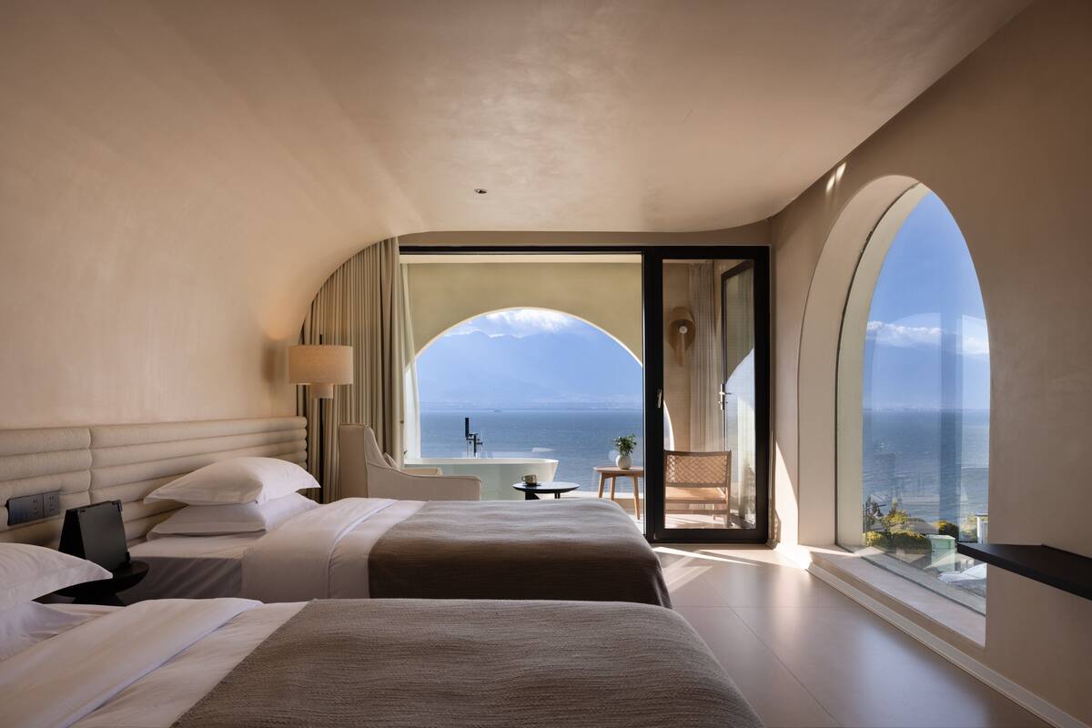 A hotel room with two beds, a view of the sea, and a balcony with a table and chair.