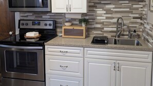 Une cuisine moderne avec des meubles blancs, des appareils en acier inoxydable, un pare-feu en carreaux et un plan de travail en bois.